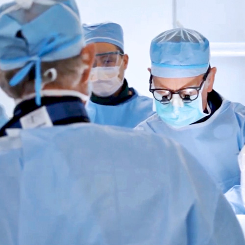 Several heart surgeons in blue gowns perform an operation in the OR