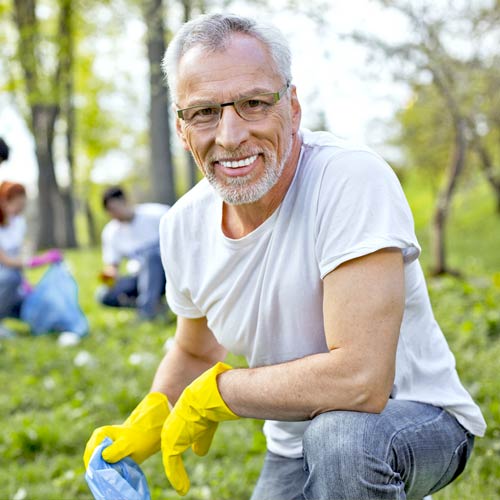 A man wearing a gray shirt and yellow gloves kneels at the park during a littler clean-up event