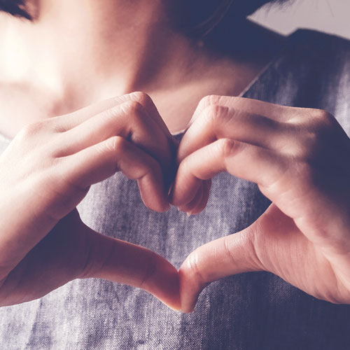 A woman in a gray shirt forms a heart with her hands
