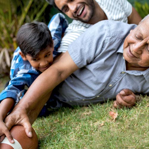 A boy, his father, and his grandfather lie on the grass, arms outstretched reaching for a football.