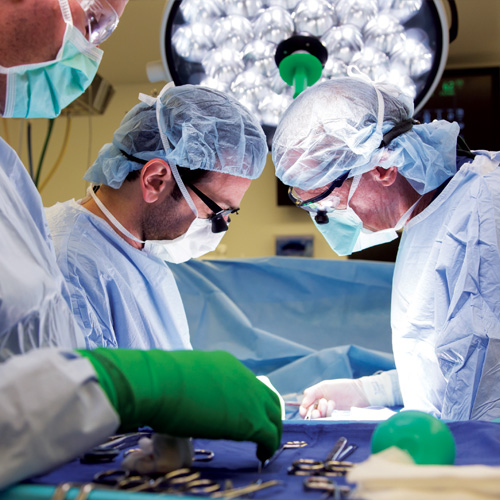 Two vascular surgeons in blue scrubs perform a heard procedure in the operating room