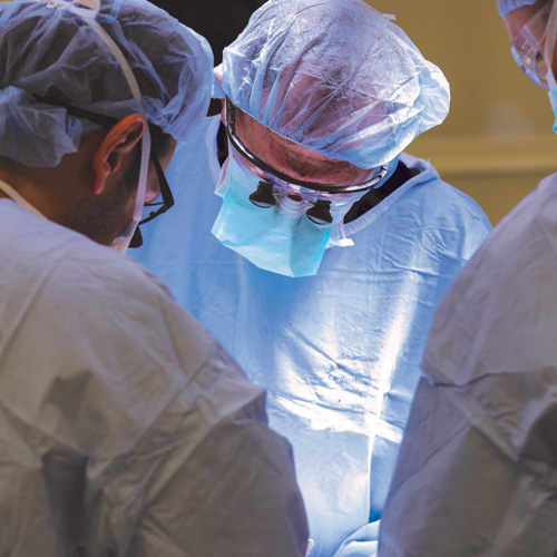 Three vascular surgeons in blue scrubs perform a heart procedure in the operating room