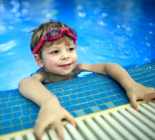 A child with swim goggles on his head about to climb out of a pool
